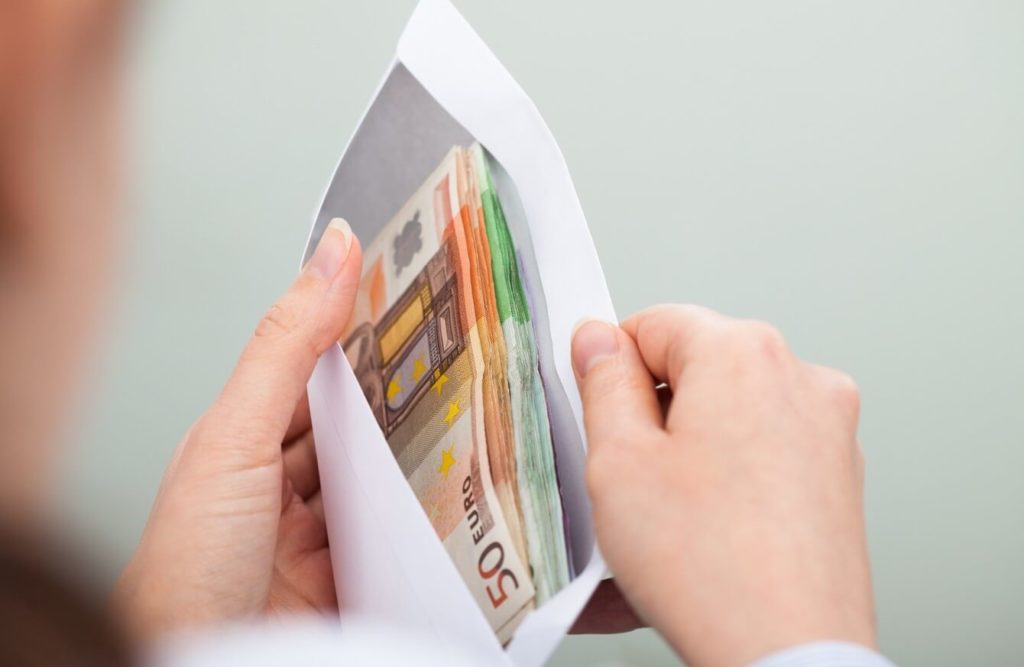 Mãos segurando um envelope cheio de euros. Custo de vida e média de salário na Irlanda