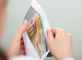 CUSTO DE VIDA E MÉDIA DE SALÁRIO NA IRLANDA Mãos segurando um envelope cheio de euros. Custo de vida e média de salário na Irlanda